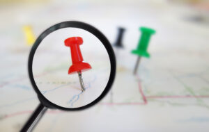 Magnifying glass closeup of push pin tacks in a map representing local seo for roofing companies